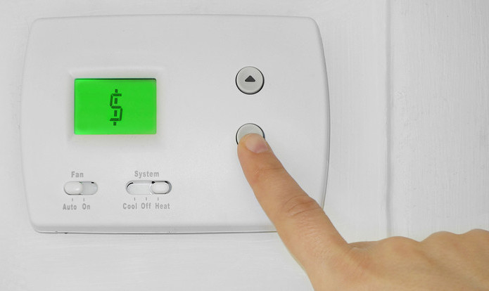 Hand adjusting a digital thermostat displaying a dollar sign, indicating energy costs related to air conditioning usage.
