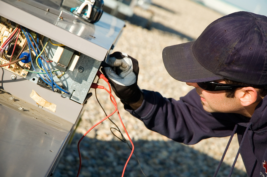 HVAC technician inspecting electrical components and wiring of an outdoor unit, demonstrating maintenance practices for optimal system efficiency.