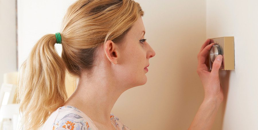 Woman adjusting thermostat.